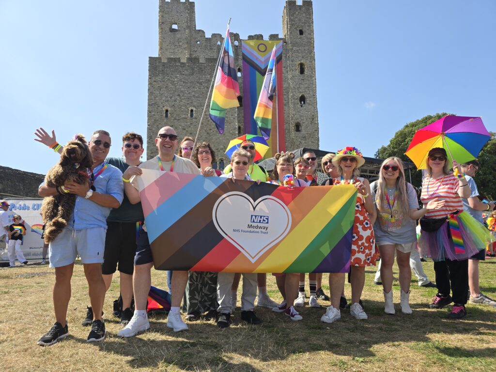 People smiling holding up a colourful banner in front of a castle