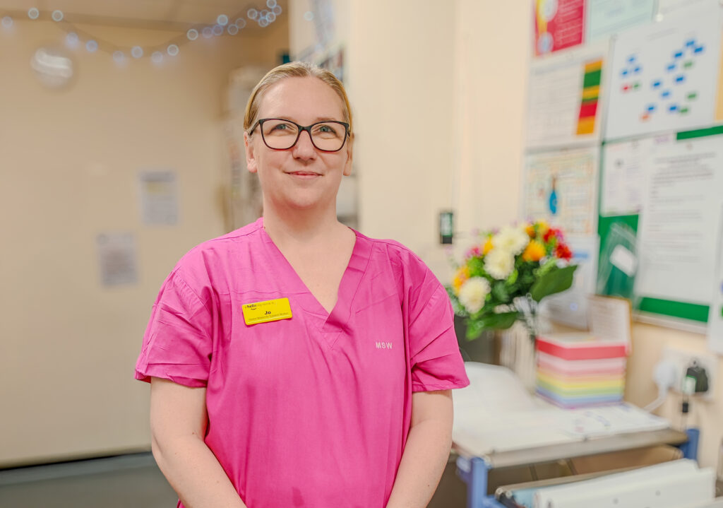 A female health worker is wearing a pink top and looking into the camera