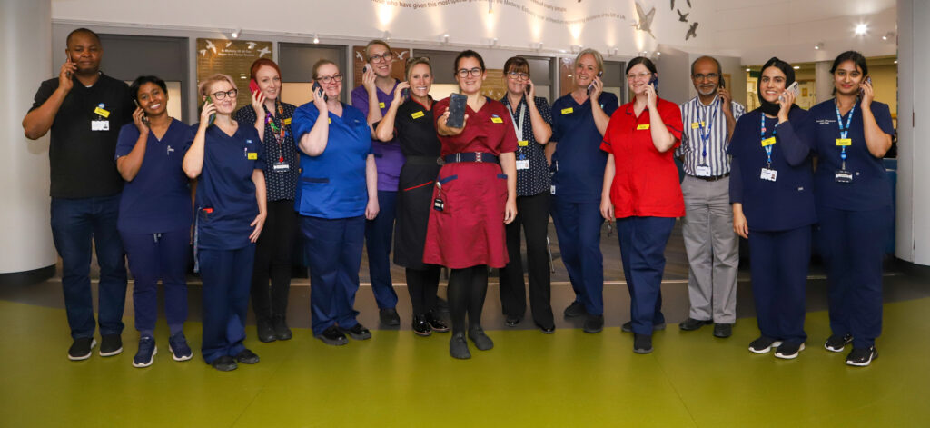 A group of healthcare professionals stand in a line holding mobile phones to their ears.